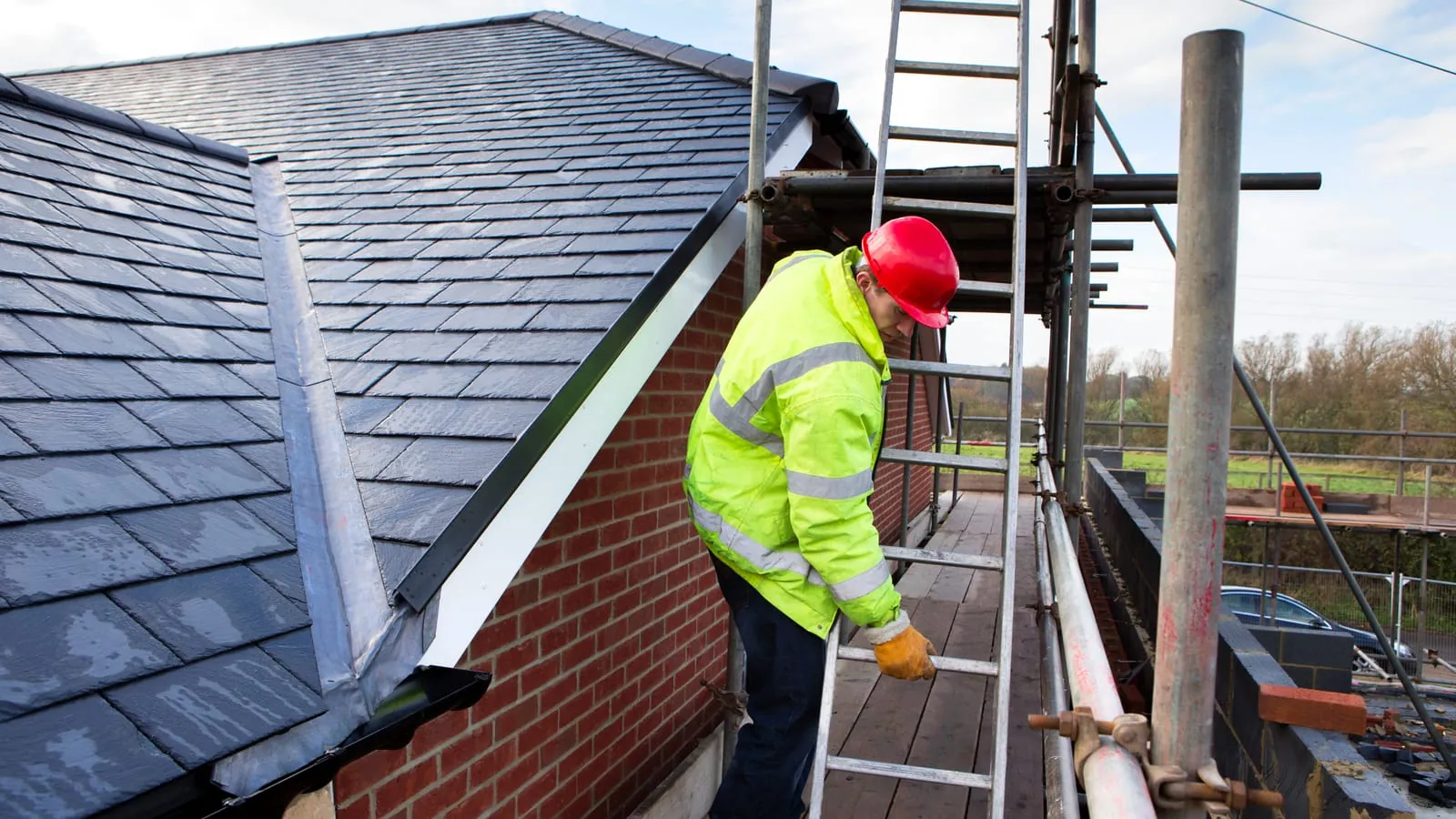 A roofer in a hi-vis jacket working from scaffolding on a slate roof