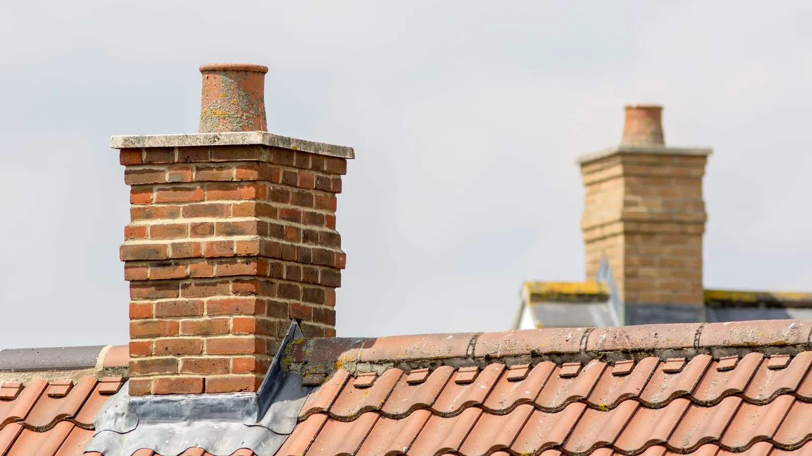 Two brick chimney stacks with clay pots and lead flashing where they meet the tiles
