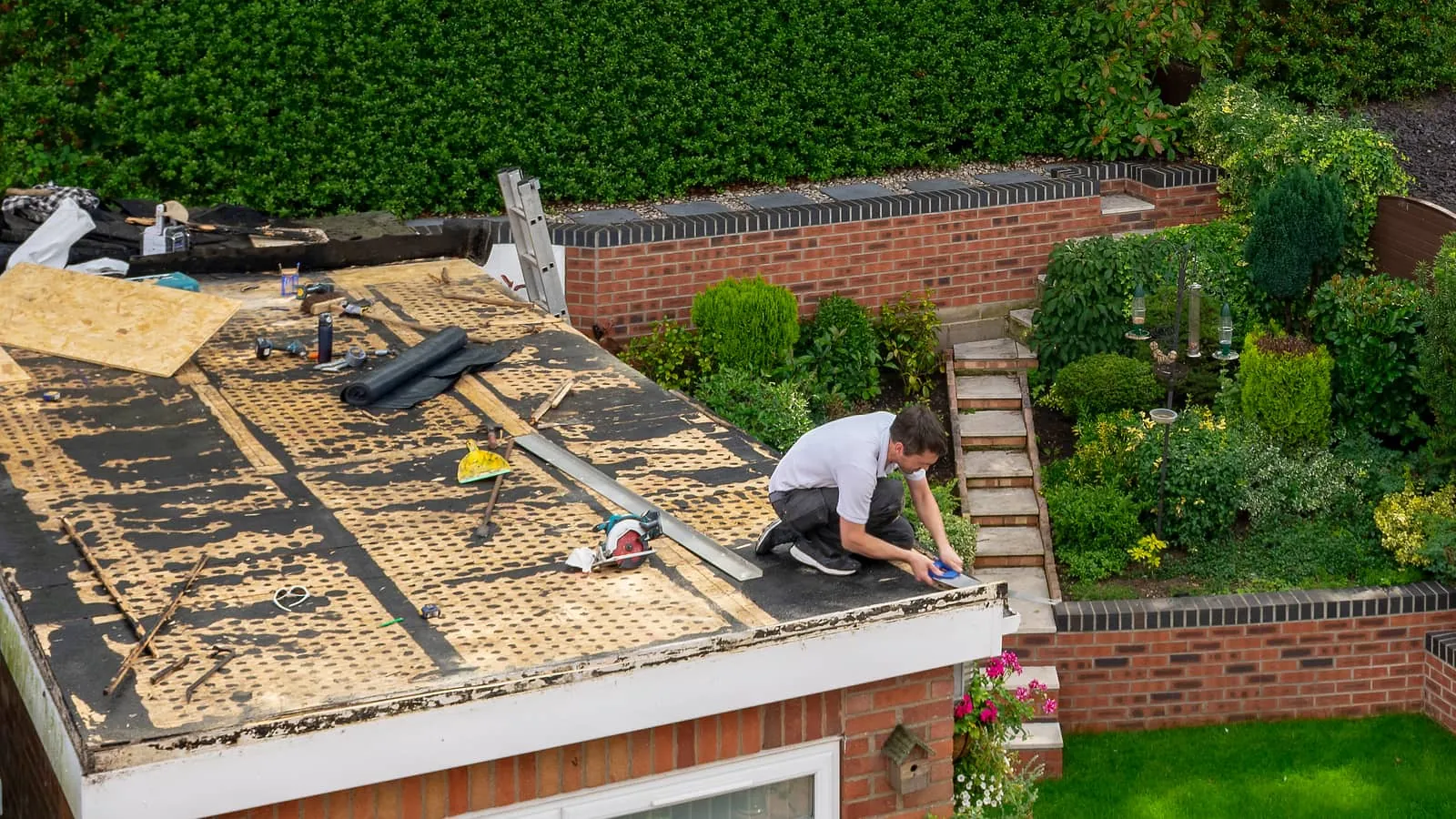 A new flat roof being laid on a brick extension above a garden