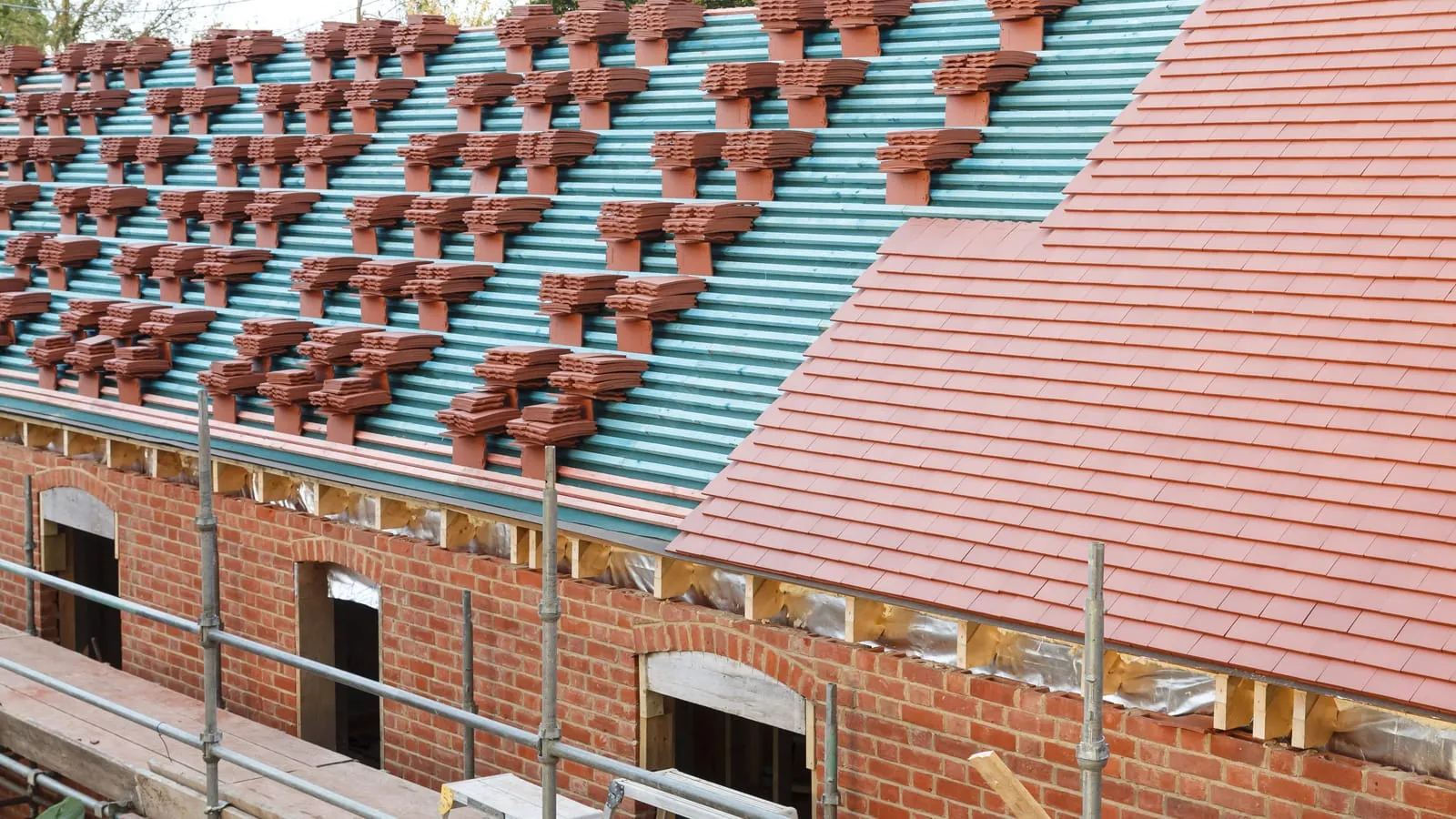 Clay roof tiles stacked in rows on new battens, part way through being laid