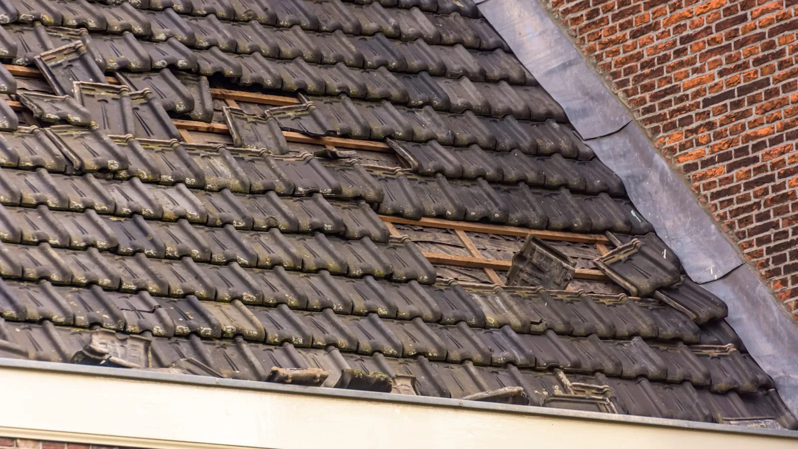 Missing tiles on a brick house exposing the battens and felt underneath